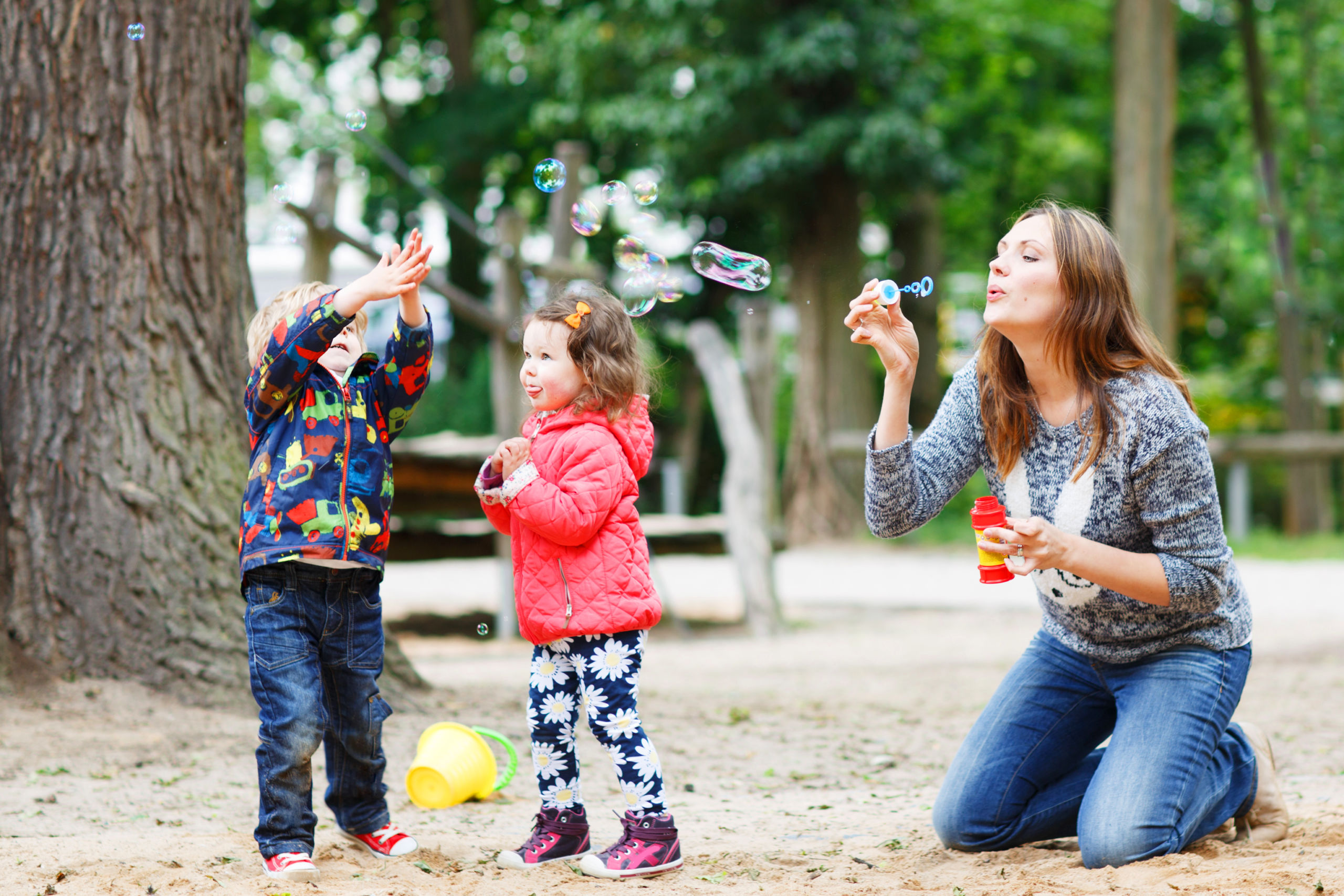 Mother blowing bubbles with children in park.
