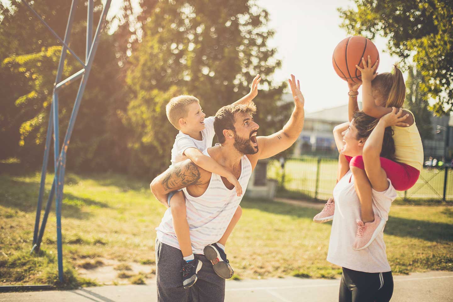 Family with children on mom and dad's shoulders playing basketball.