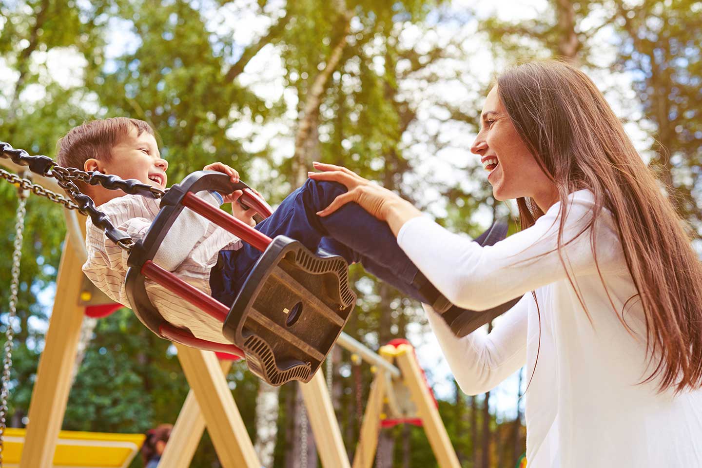 Woman pushing a child in a swing on playground.